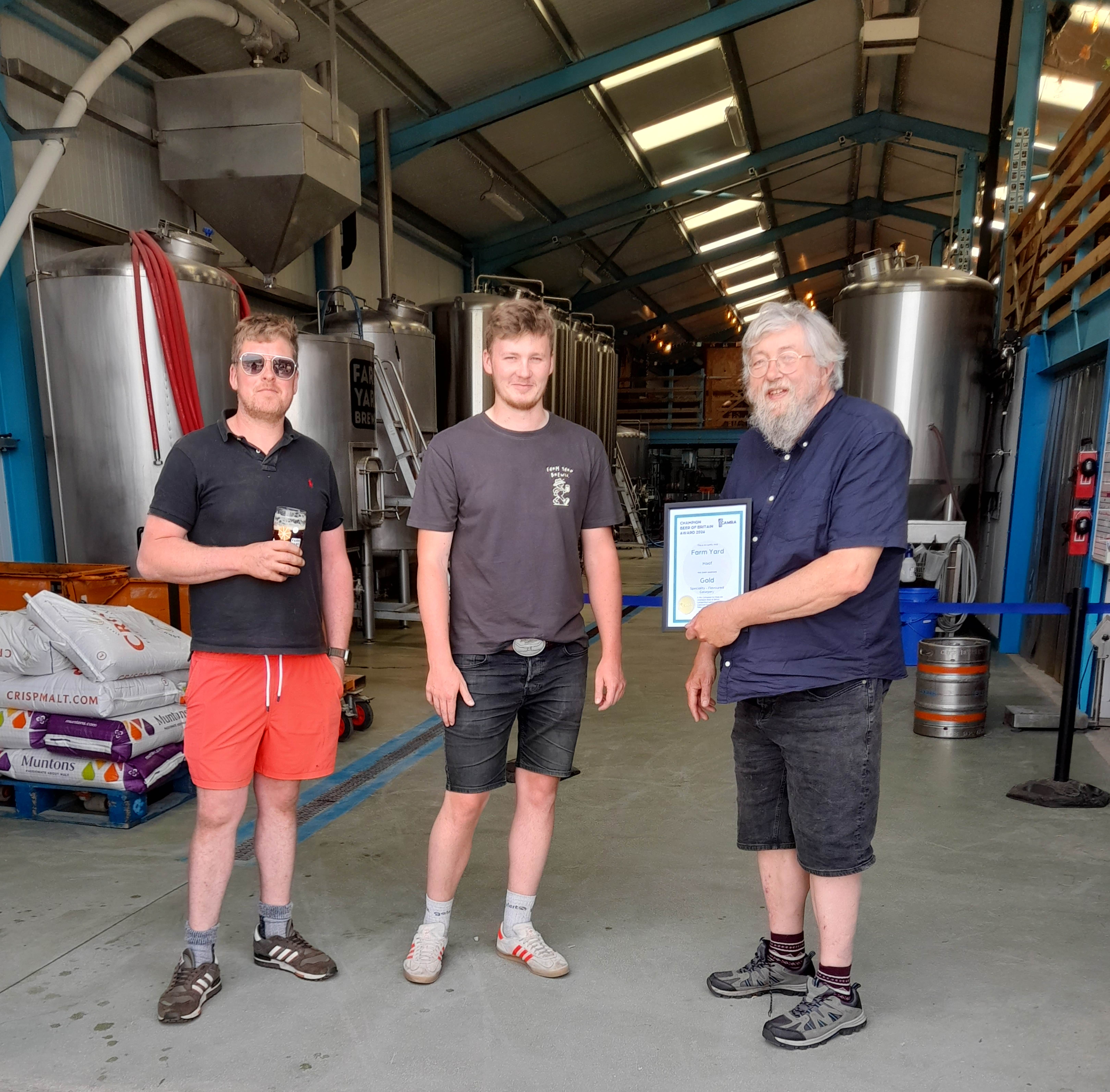 Three people in a brewery with a framed certificate