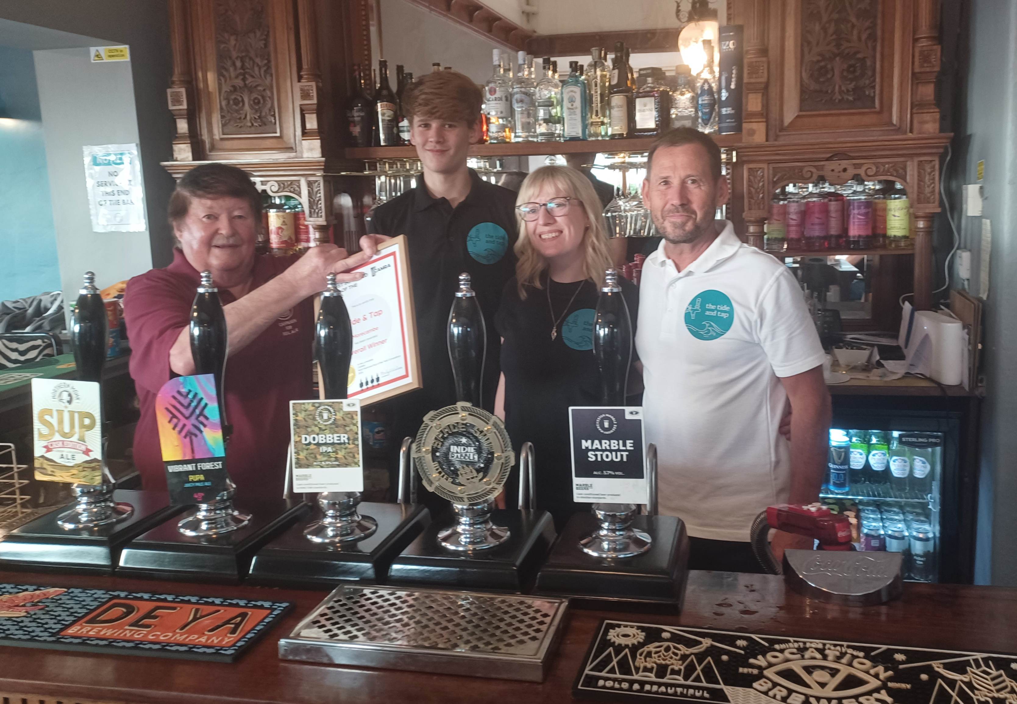 Three people in a bar with a framed certificate